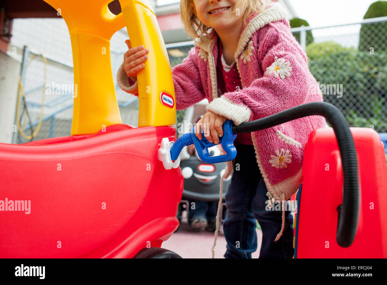 Ein junges Mädchen pumpt Kraftstoff in ihrem Little Tikes Auto. Stockfoto