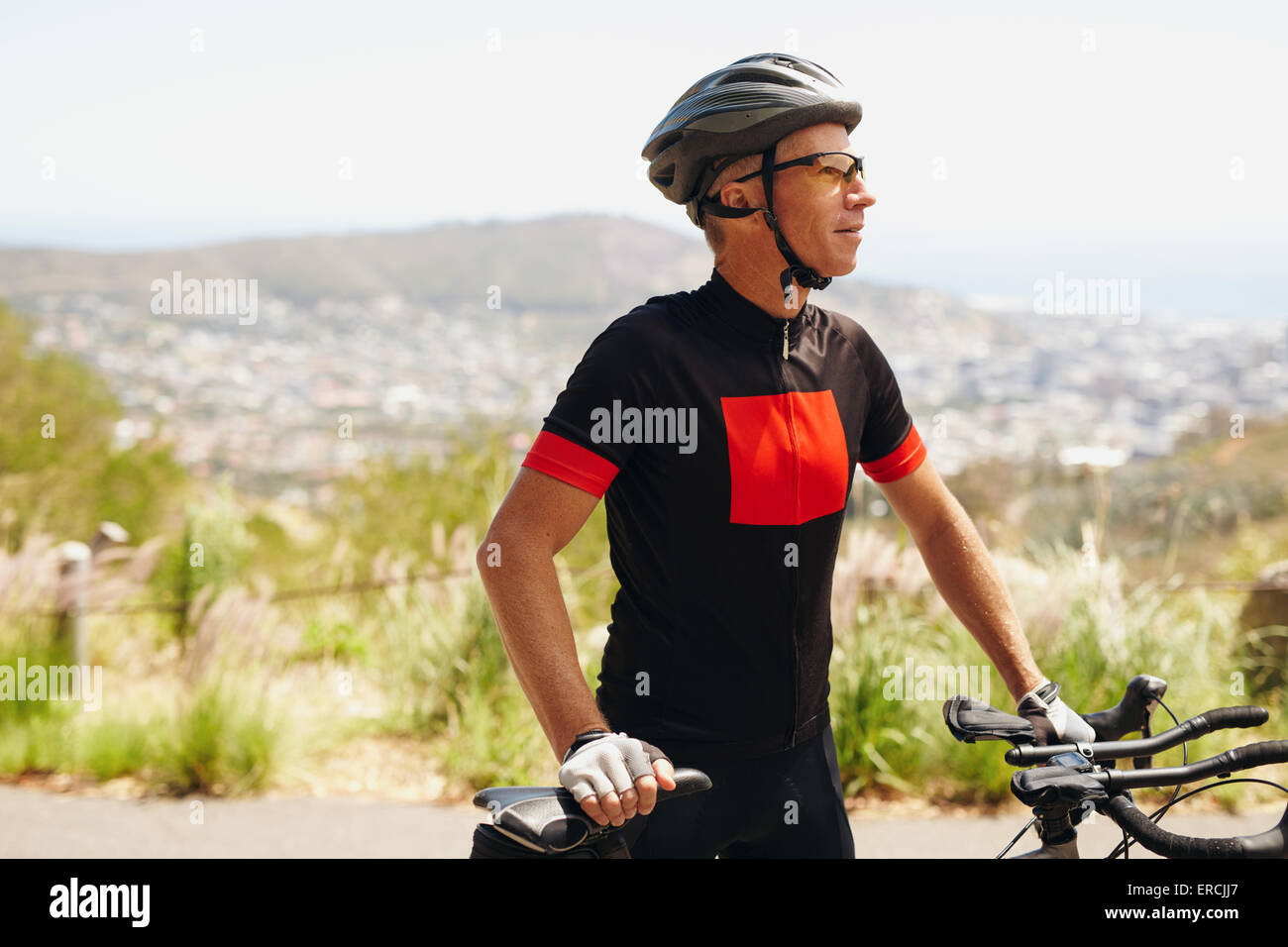 Junge Mann mit Helm und Sonnenbrille steht mit seinem Fahrrad wegsehen. Männliche Radfahrer Ausbildung auf Land. Stockfoto