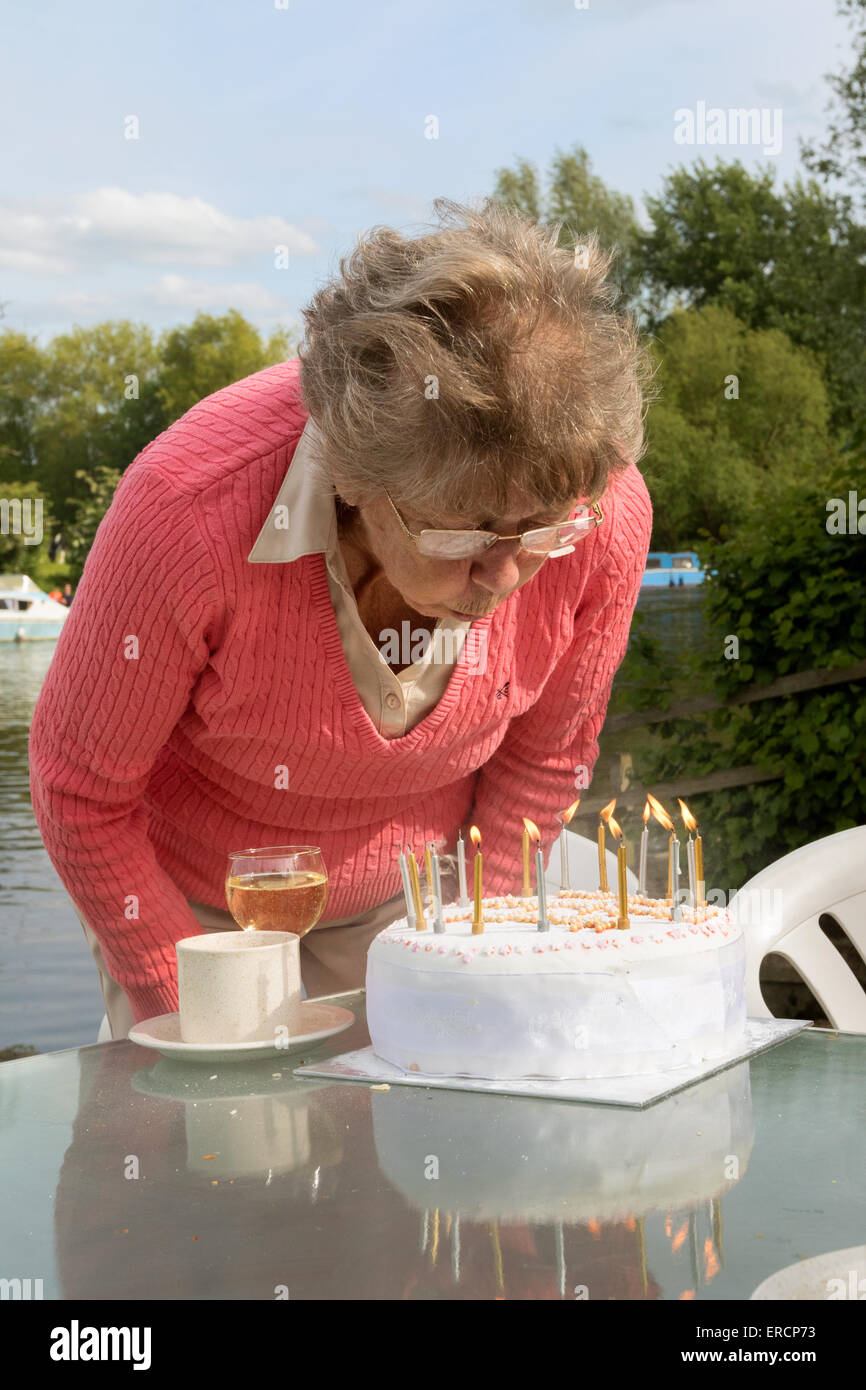 Eine Reife im Ruhestand Seniorin Ausblasen der Kerzen auf ihrem Geburtstagskuchen, UK Stockfoto