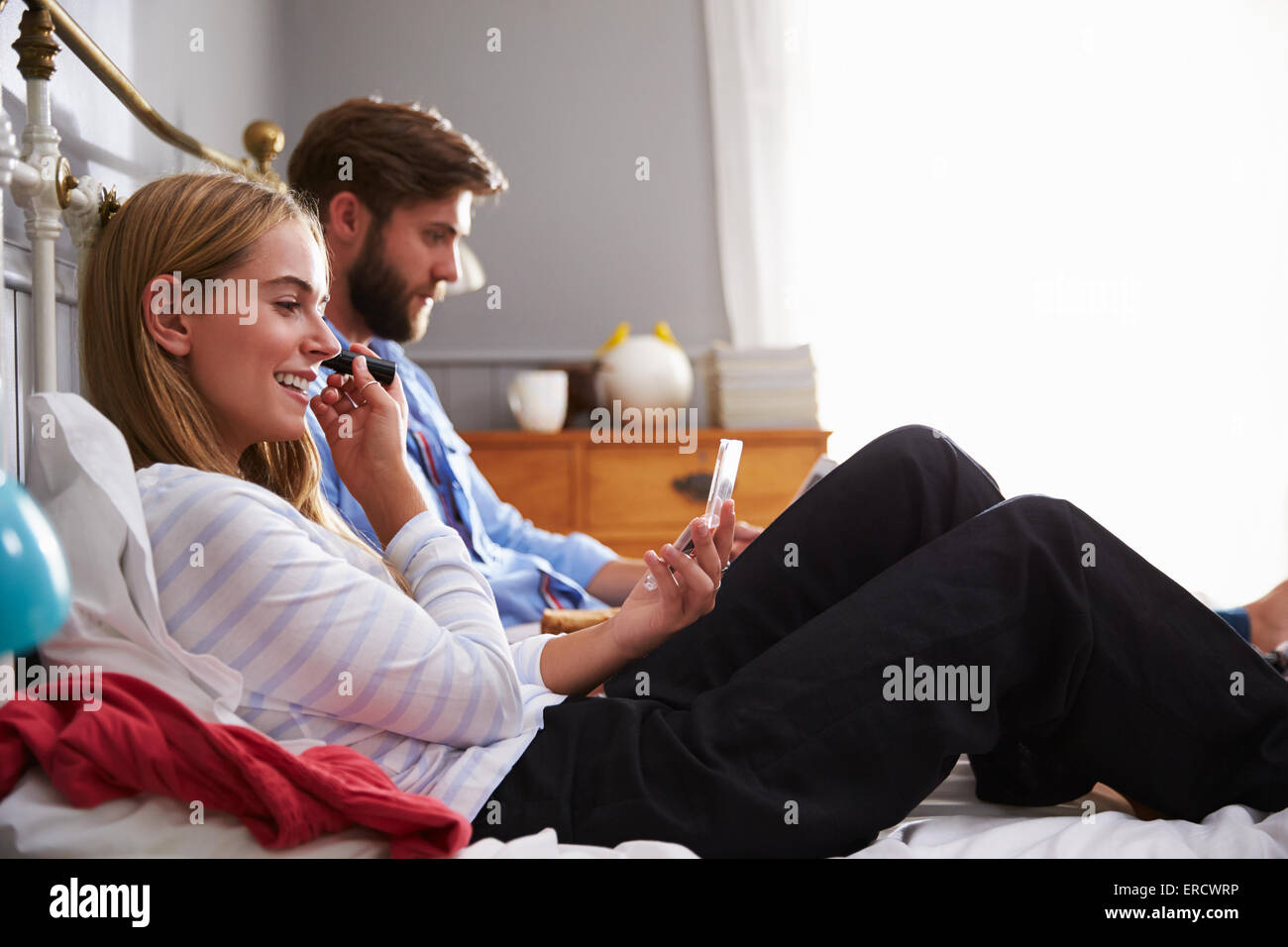 Frau legt auf Make Up als Mann nutzt digitale Tablet im Schlafzimmer Stockfoto