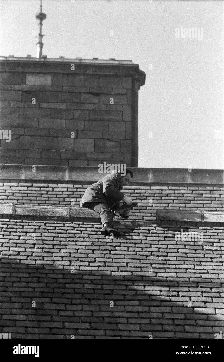 Demonstrant Keith Lomax gesehen hier auf dem Dach des Rathauses von Rochdale entfernen Dachziegel aus Protest gegen die Länge der Zeit, dass er und seine Familie mussten warten, bis ihr Dach fixiert das Polizei warten unten zu verhaften Herr Lomax. 28. März 1975 Stockfoto
