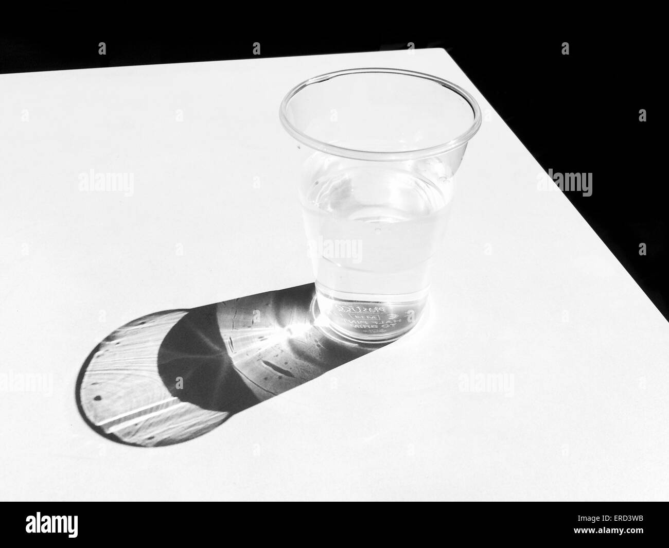 Sonne, wirft einen Schatten von einem Becher Wasser auf einer weißen Tischplatte im Vereinigten Königreich Stockfoto