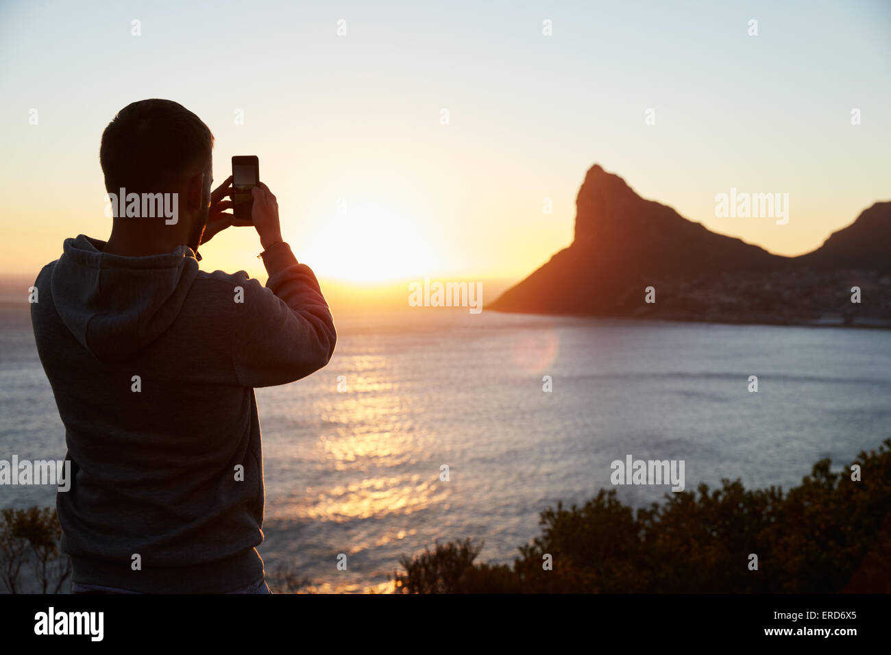 Mann, die Aufnahme der Sonne Einstellung über Meer auf dem Handy Stockfoto