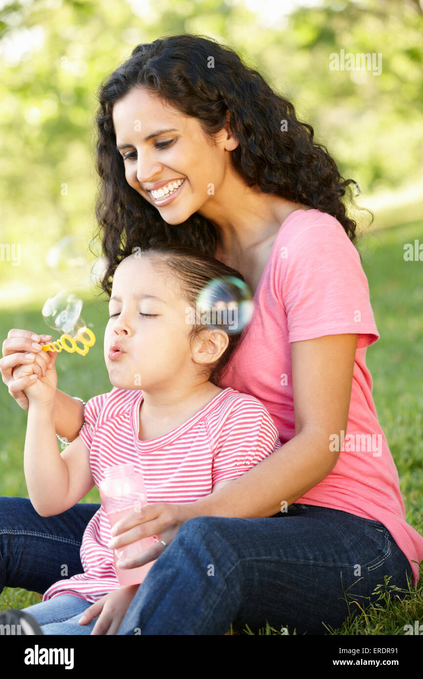 Hispanic Mutter und Tochter bläst BubblesIn Park Stockfoto