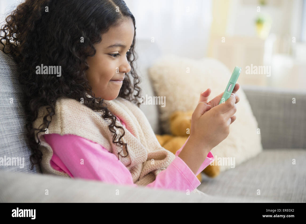 Gemischte Rassen Mädchen SMS mit Handy auf sofa Stockfoto