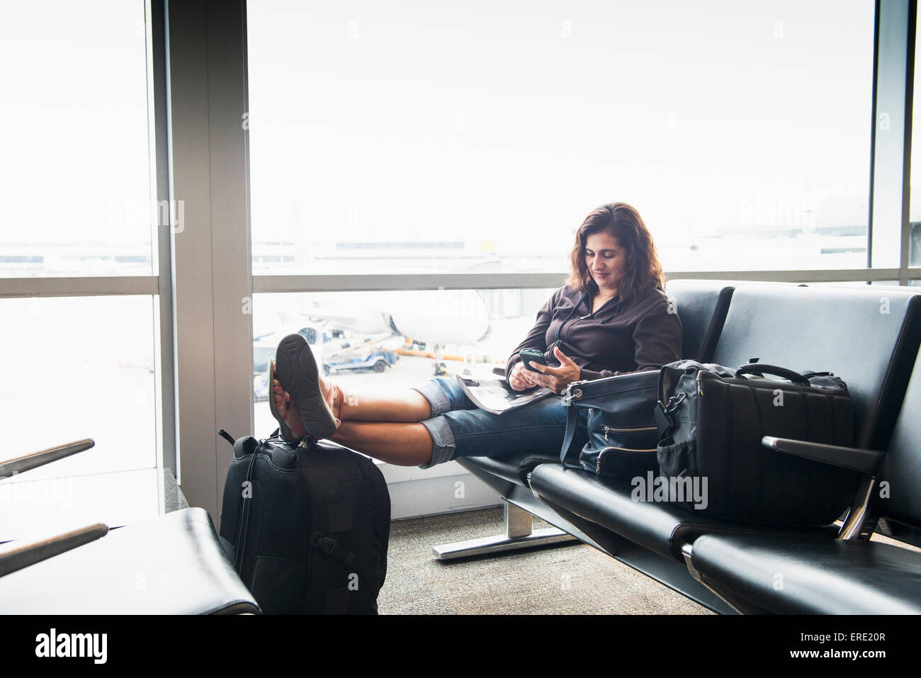 Hispanic Frau SMS auf Handy in Flughafen Stockfoto