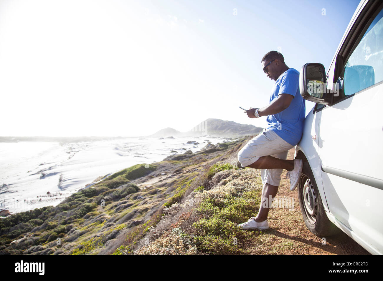 Schwarzer Mann SMS Handy in der Nähe von Auto an Küste Stockfoto