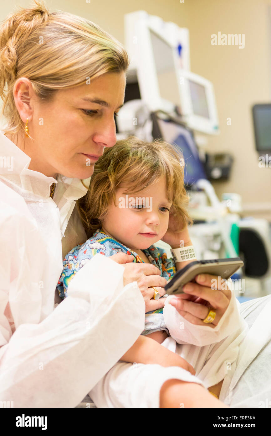Kaukasische Mutter und Sohn SMS auf Handy im Krankenhaus Stockfoto
