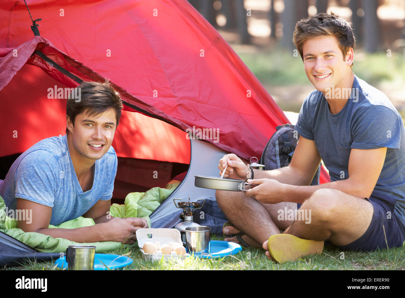 Zwei junge Männer auf Campingkocher vor Zelt kochen Stockfoto