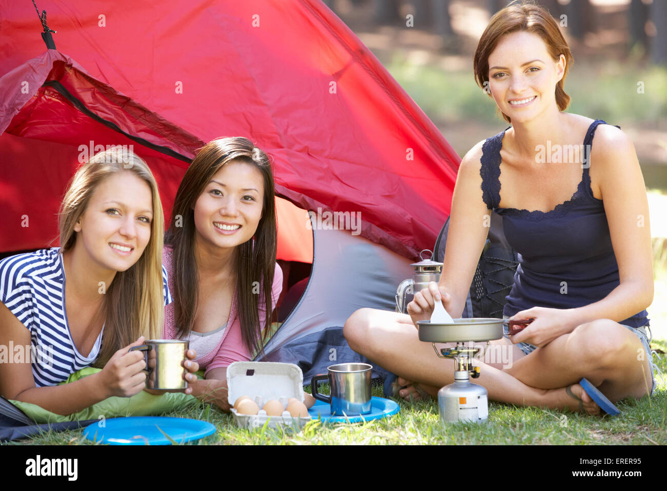 Drei junge Frauen auf Campingkocher vor Zelt kochen Stockfoto