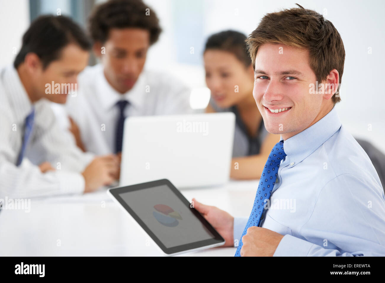 Porträt von männlichen Executive mit Tablet-PC mit Office-Meeting im Hintergrund Stockfoto