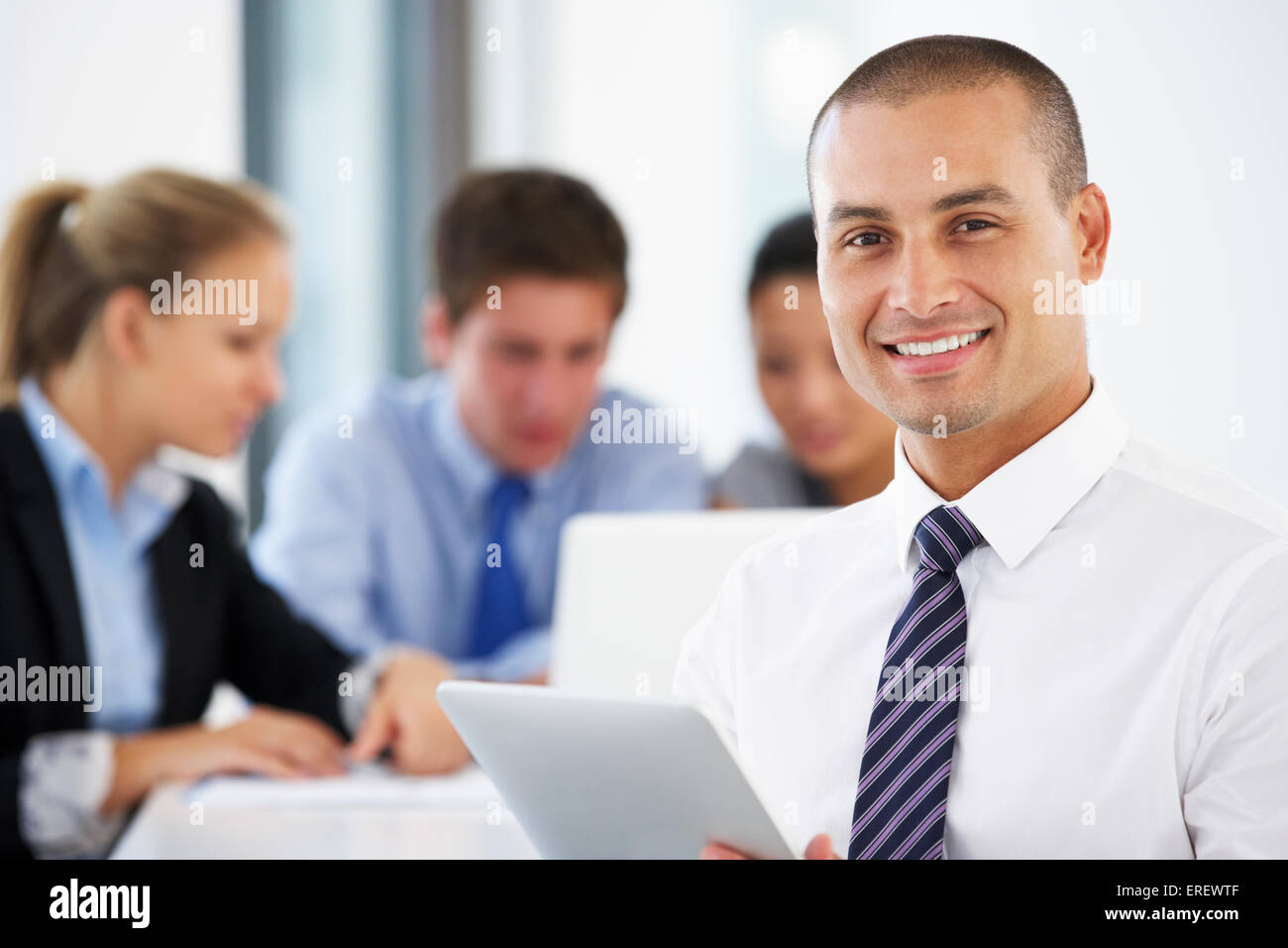 Porträt von männlichen Executive mit Tablet-PC mit Office-Meeting im Hintergrund Stockfoto
