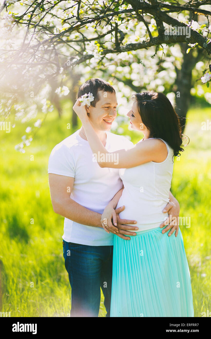Porträt von glücklich schwanger Familie. Schwangere Frau und Mann in blühenden Frühling Garten in sonniger Tag. Zwei verliebte. Stockfoto