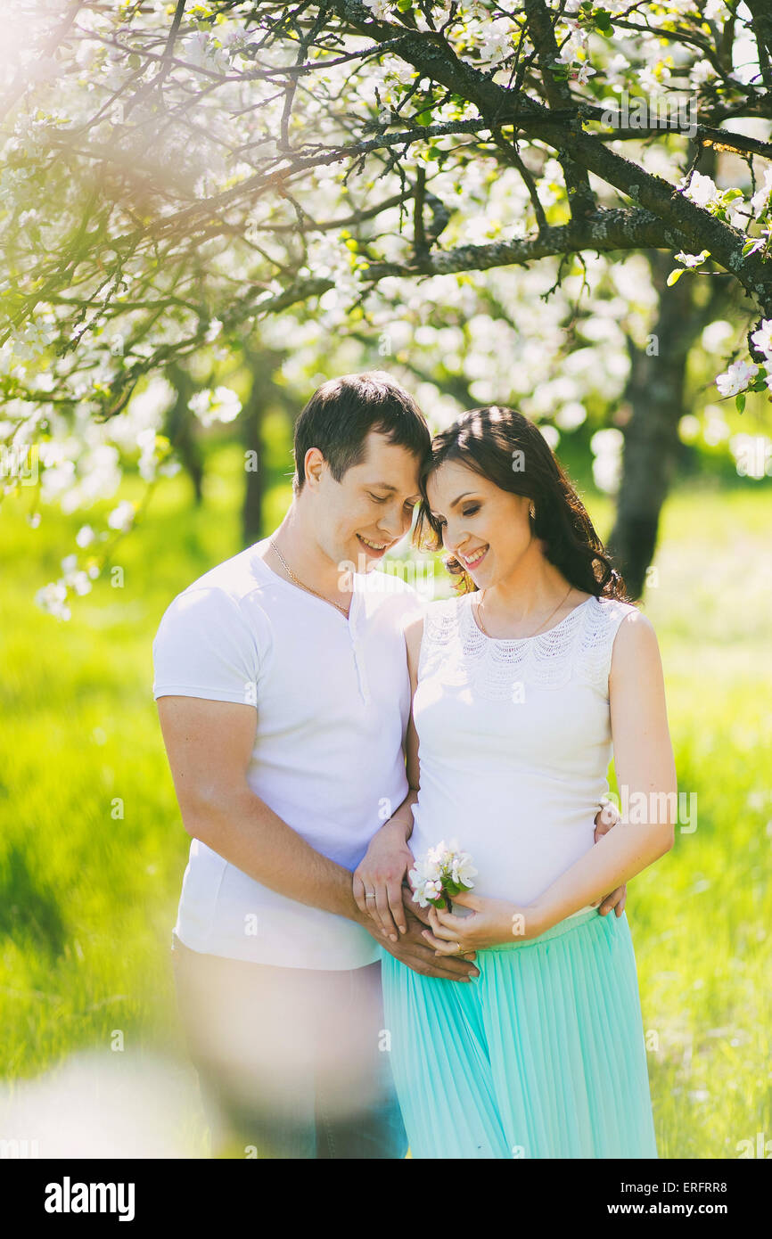Porträt von glücklich schwanger Familie. Schwangere Frau und Mann in blühenden Frühling Garten in sonniger Tag. Zwei verliebte. Stockfoto