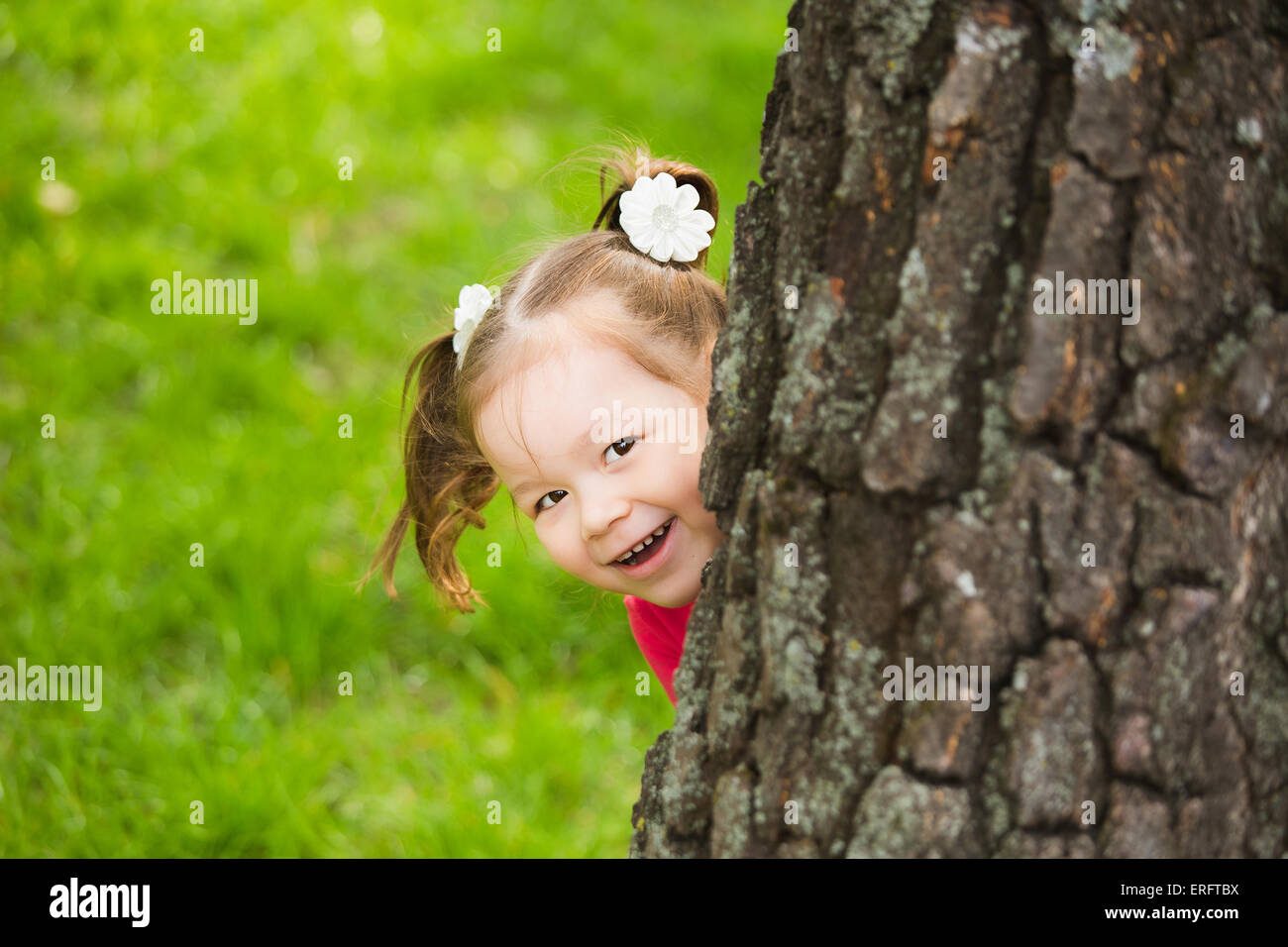 niedliche kleine Mädchen versteckt sich hinter riesigen Baum. Kinder Porträt Blick in die Kamera Stockfoto