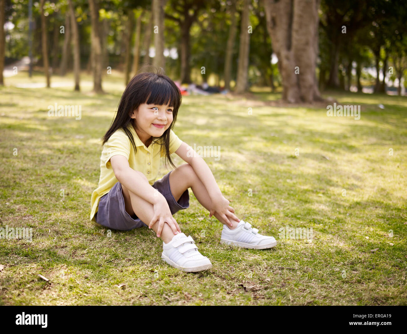 kleine Asiatin sitzt auf dem Rasen im Park. Stockfoto