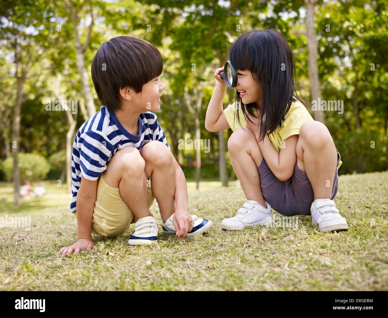 kleine Asiatin Blick auf kleinen asiatischen Jungen durch eine Lupe im Freien in einem Park. Stockfoto