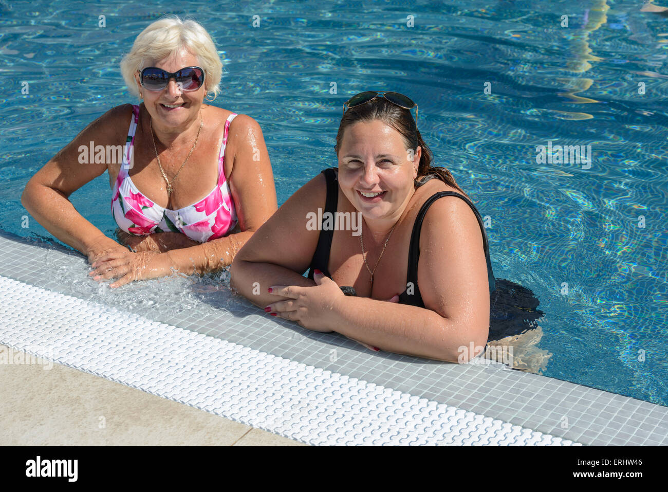 Zwei gebräunte lächelnde Frauen, ältere Blonde Mutter und Mitte Erwachsene Brünette Tochter stehen in strahlend blauen Wasser am Rand des Stockfoto