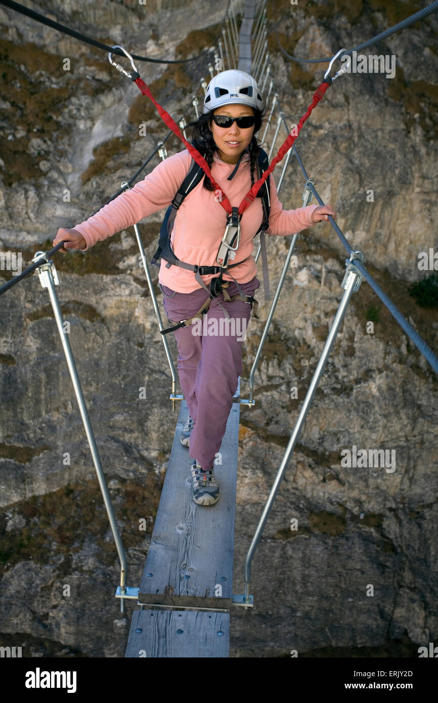 Eine junge Frau auf einer Brücke zu Fuß während der Teilnahme an den Sport Via Ferrata im Val D'isere, Savoie. Stockfoto
