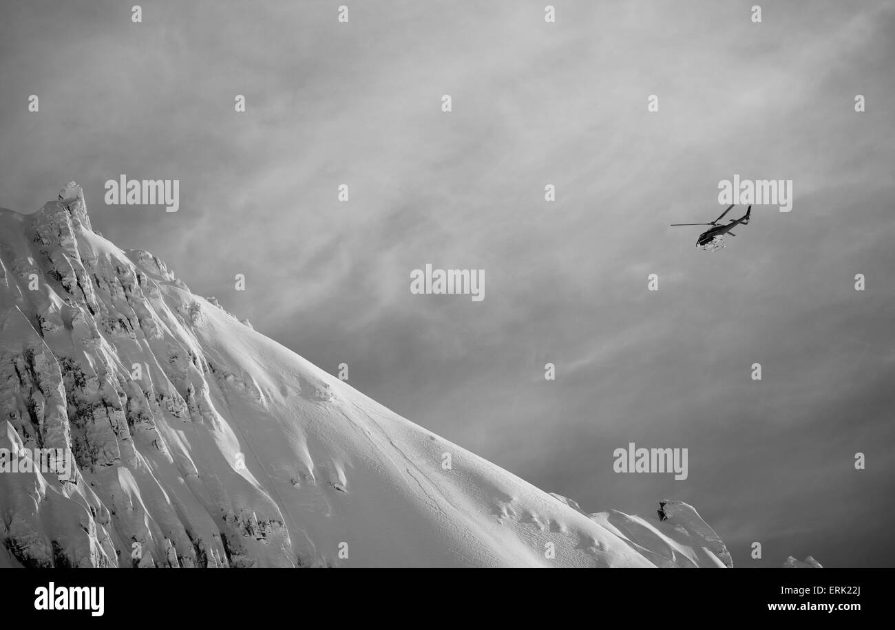 Hubschrauber fliegt durch bewölktem Himmel nach einem verschneiten Berggipfel; Neuseeland Stockfoto