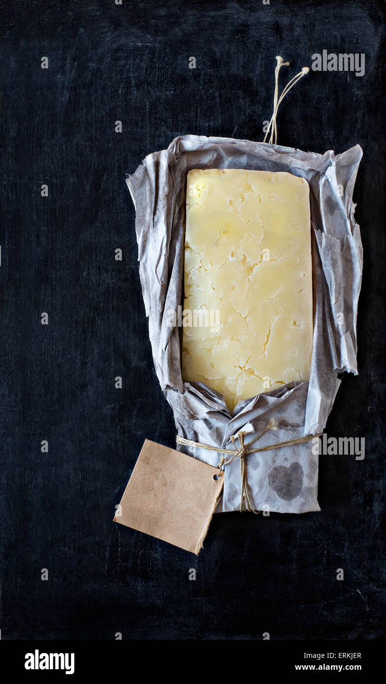 Ein Block von englischen reifer Cheddar-Käse eingewickelt in rustikalen Papier mit einem leeren Etikett auf einer Tafel. Stockfoto