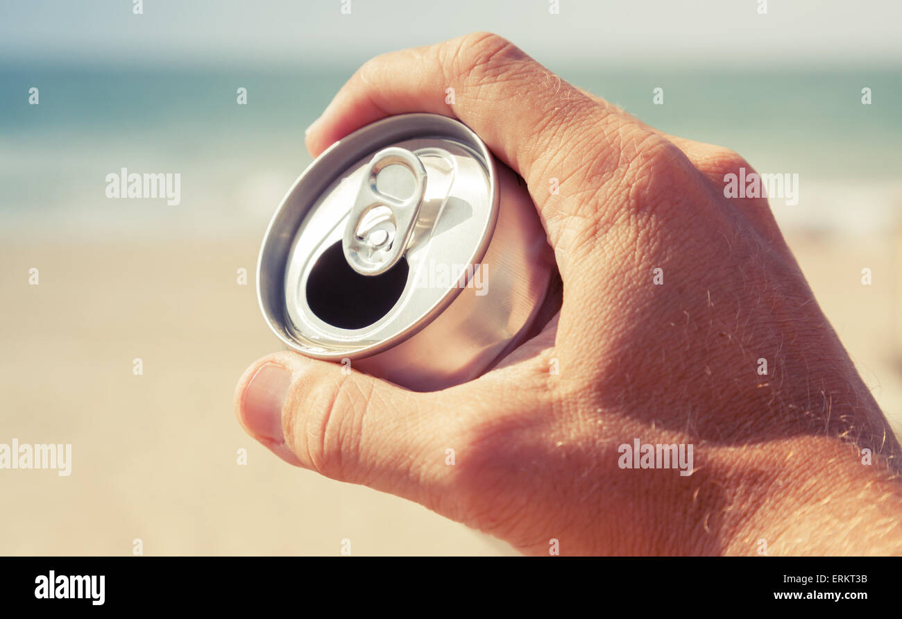Aluminium kann Bier in männlicher Hand mit verschwommenen Strand und Meer auf einem Hintergrund, getönten Vintage Foto, Retro-tonale Foto Filter Corr Stockfoto