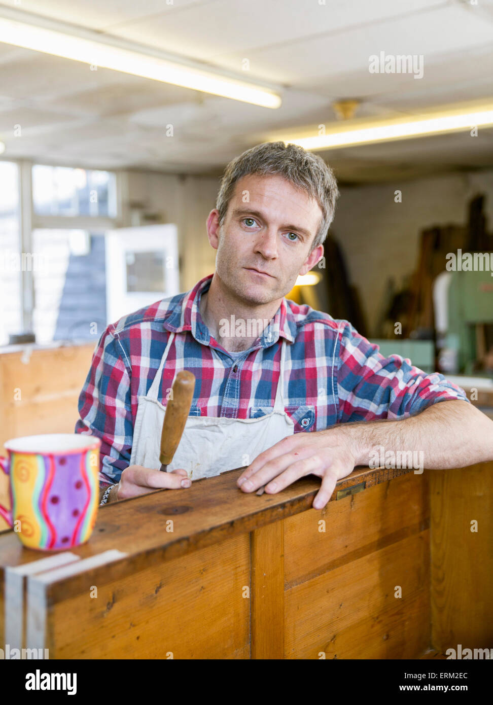 Eine antike Möbelrestaurator, ein Mann stützte sich auf ein Möbelstück hält eine Hand-Werkzeug. Stockfoto