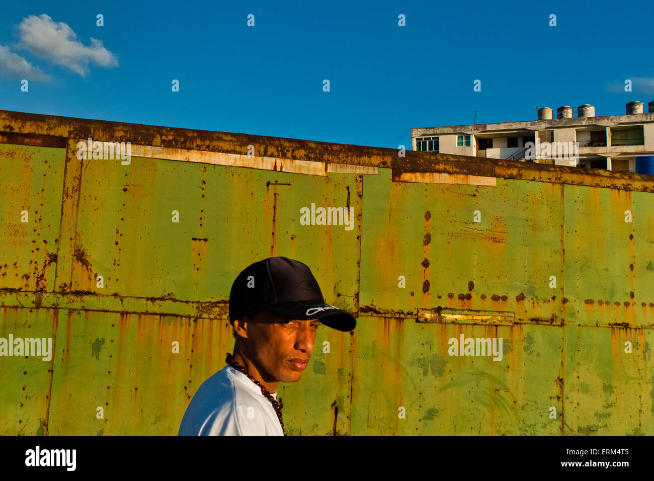 Ein junge kubanische Mann, trägt eine Baseballkappe, geht vor einem rostigen Container in Alamar, Havanna, Kuba. Stockfoto
