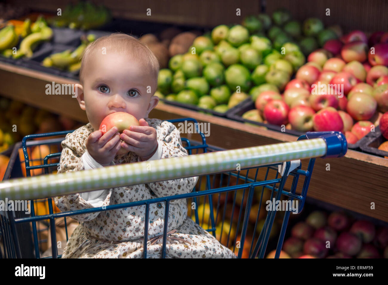 Niedliche Baby in einem Einkaufswagen einen Apfel essen Stockfoto