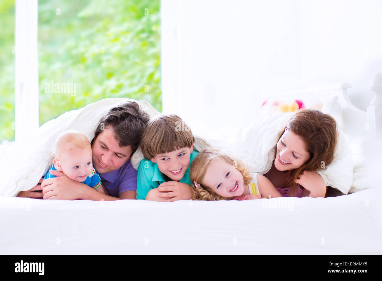 Glückliche Großfamilie, junge Eltern mit drei Kindern, lachen, junge, Kleinkind Mädchen und entzückende kleine Baby tragen bunte Schlafanzüge Stockfoto