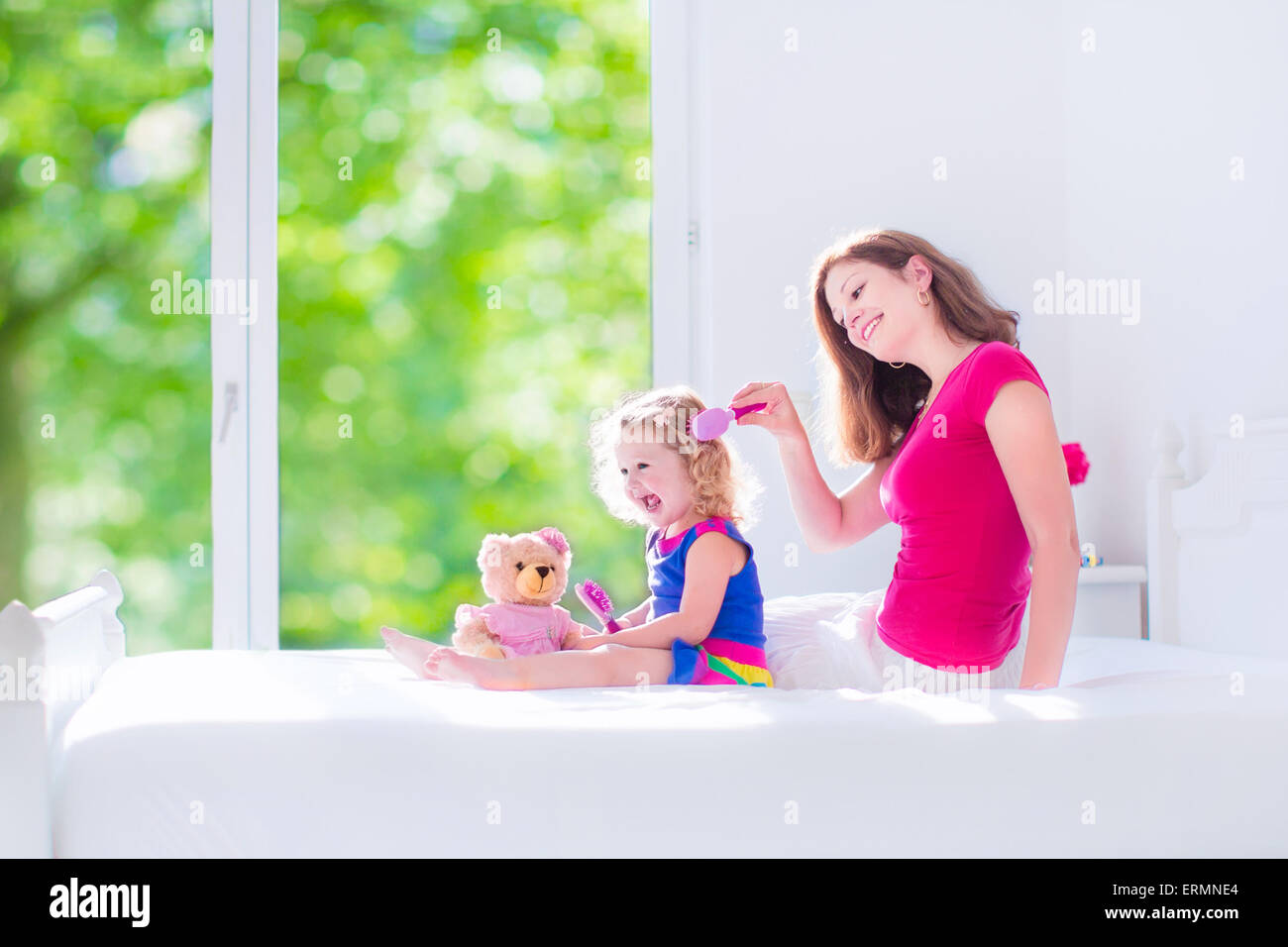 Glückliche Familie, schöne junge Mutter und ihre entzückende Tochter, süß lustig Mädchen mit dem lockigen Haar Bürsten Haare Stockfoto
