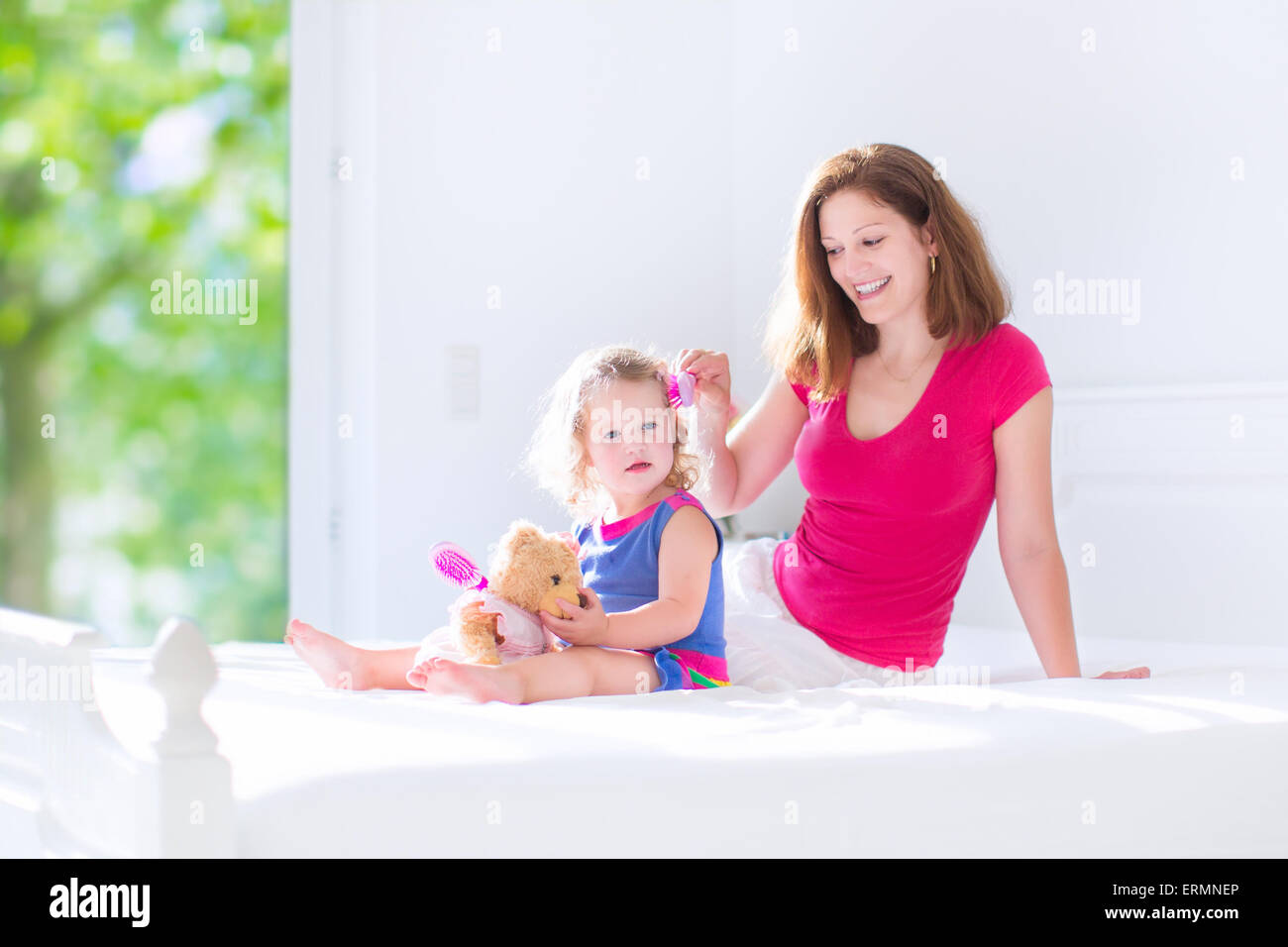 Glückliche Familie, schöne junge Mutter und ihre entzückende Tochter, süß lustig Mädchen mit dem lockigen Haar Bürsten Haare Stockfoto