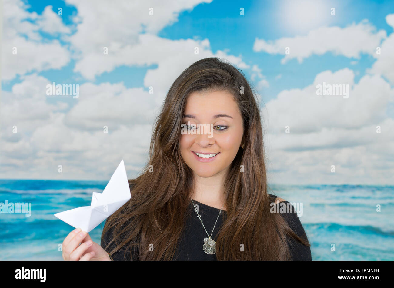 Brünette hält eine Origami-Papier-Figur vor ozeanische Wolke Hintergrund Stockfoto