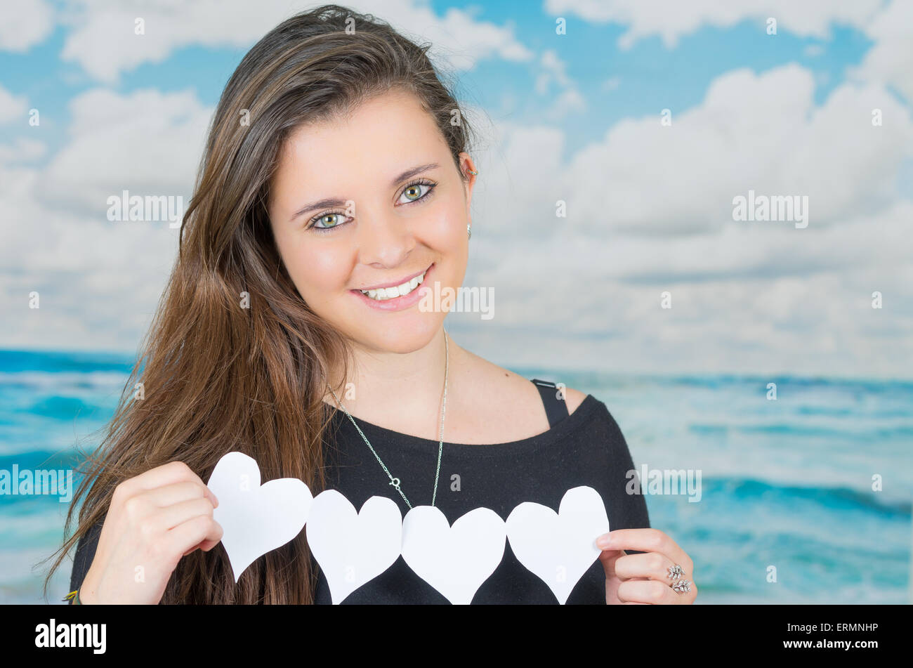 Brünette hält eine Origami-Herzform-Papier-Figur vor der ozeanische Wolke Hintergrund Stockfoto