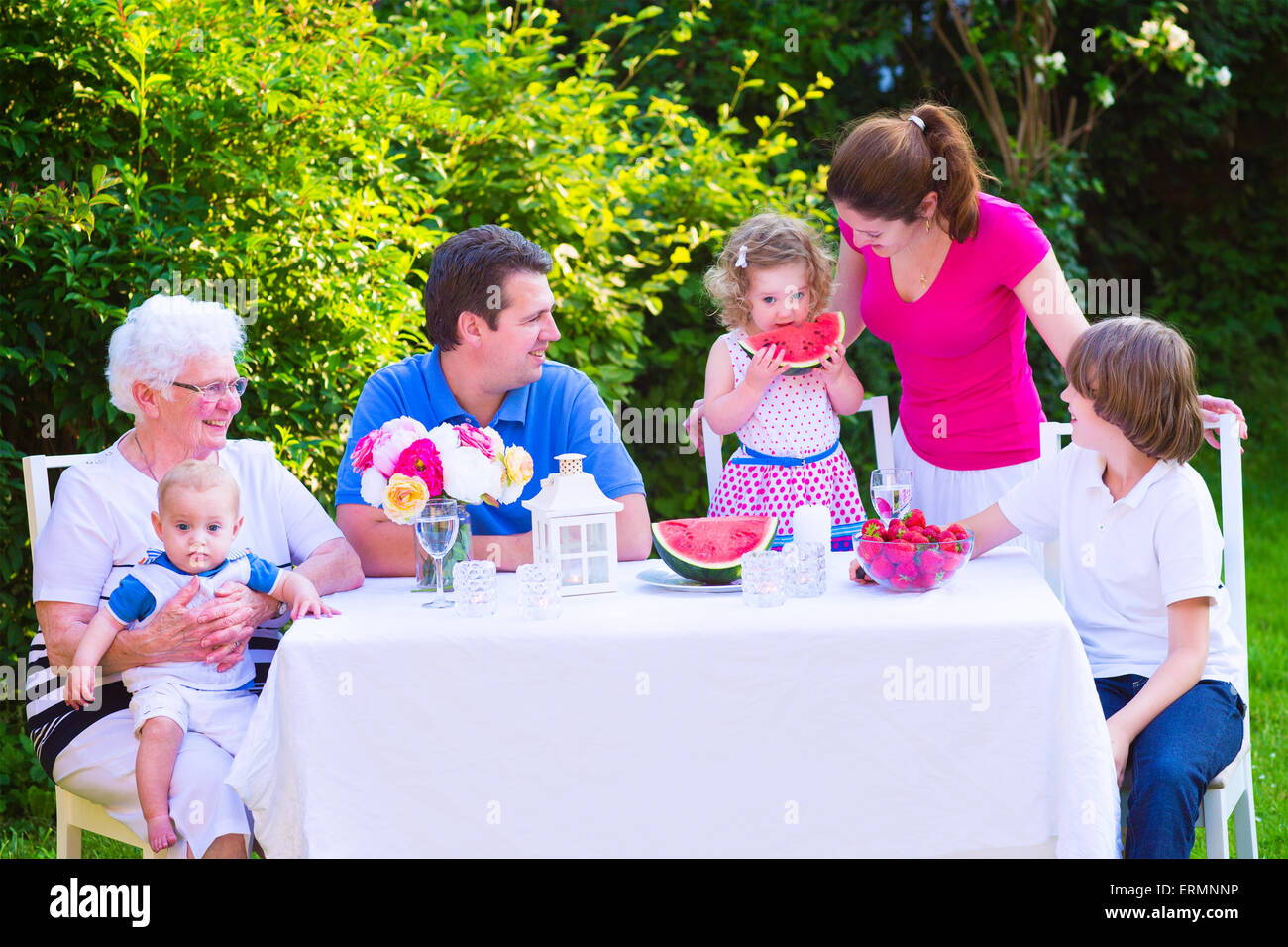Glückliche Großfamilie - junge Mutter und Vater mit Kindern genießen Mittagessen mit Großmutter Verzehr von Obst, Wassermelone im Garten Stockfoto