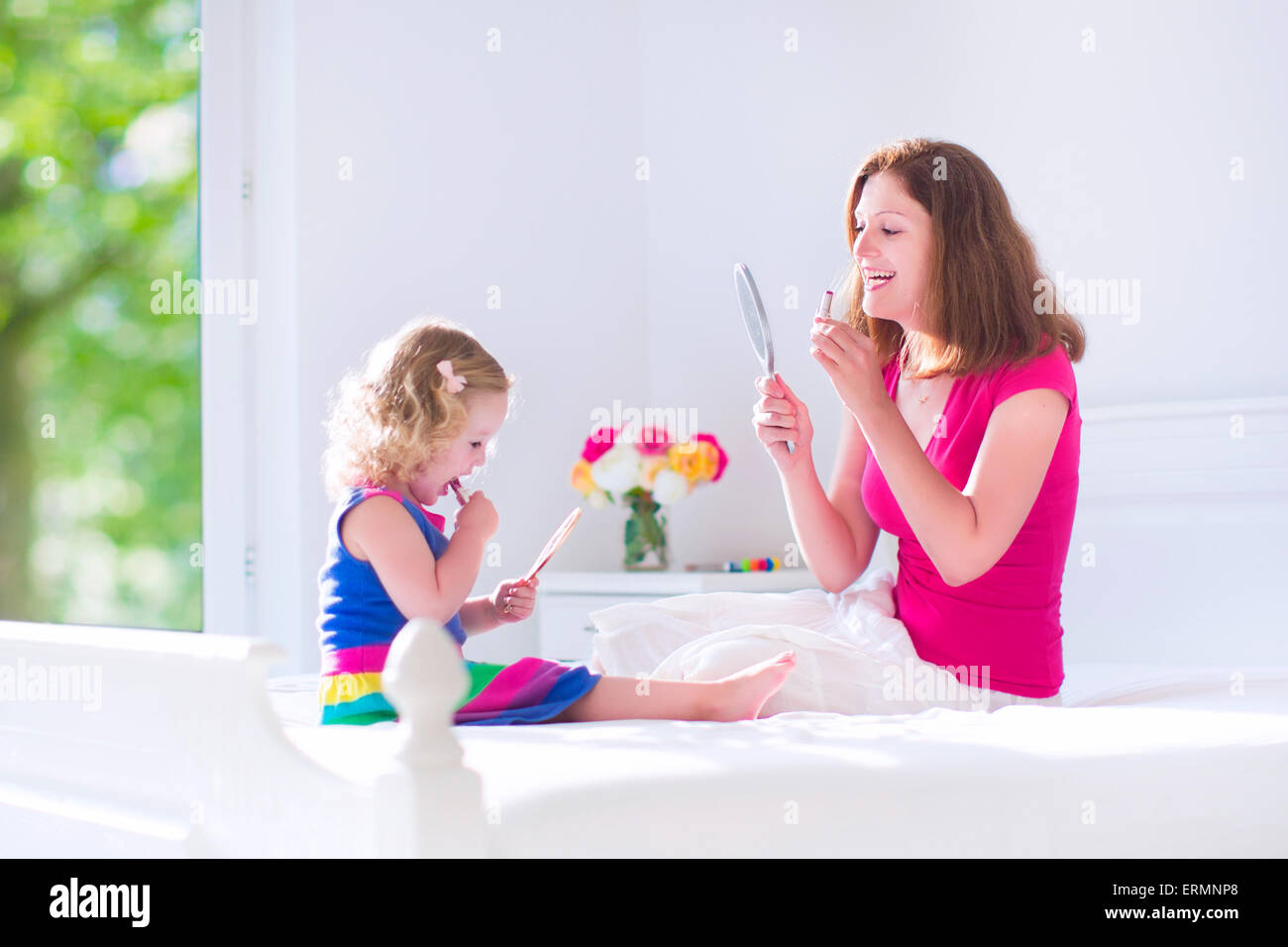 Gerne schöne junge Mutter und ihre entzückende Tochter, Anwendung von Make-up, Lippenstift, Blick in Hand Spiegel Stockfoto