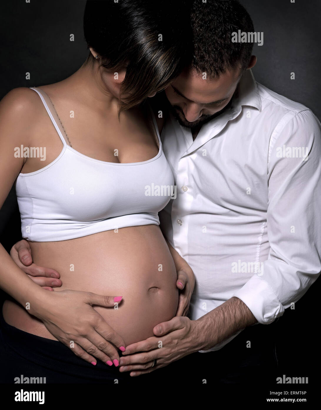 Schöne sanfte schwangere Frau und ihr liebevoller Ehemann zärtlich berühren und Blick am Bauch auf schwarzem Hintergrund Stockfoto