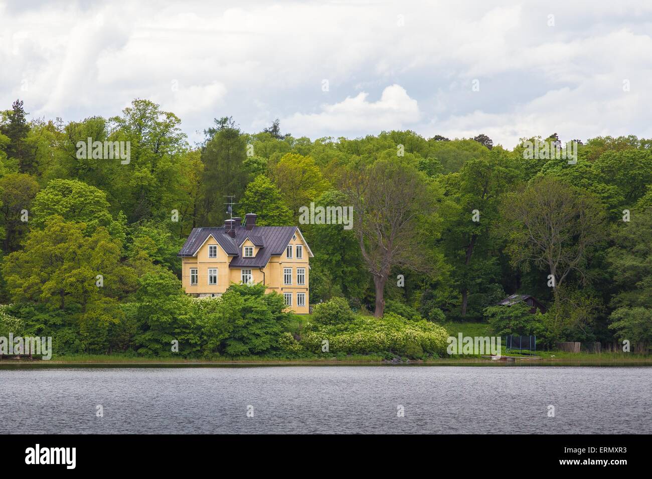 Gelbes Haus in der Nähe von einem See mit einem wolkigen Himmel im Hintergrund Stockfoto