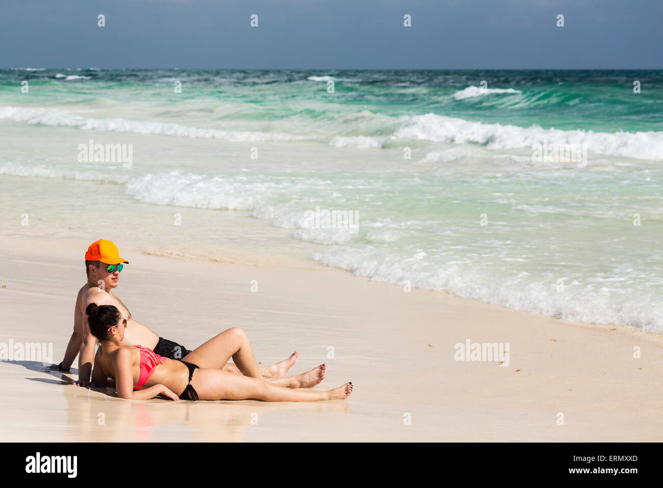 Paar Verlegung und sitzen auf dem sandigen Strand mit Wellen hereinkommen und blauer Himmel; Tulum, Quintana Roo, Mexiko Stockfoto