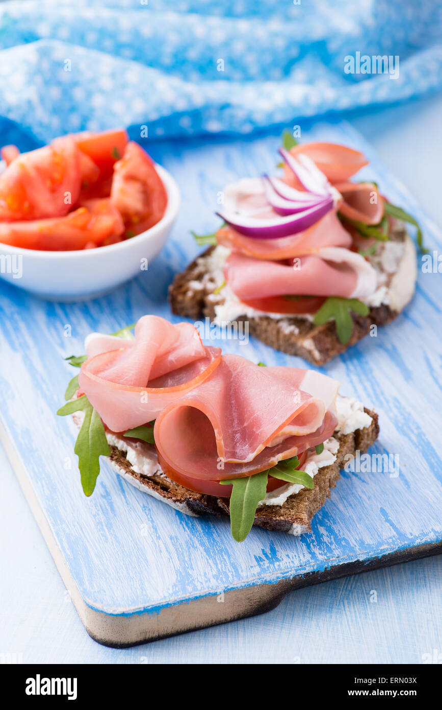 Belegte Brötchen mit Schinken, Tomaten und Rucola auf blauem Hintergrund, selektiven Fokus Stockfoto