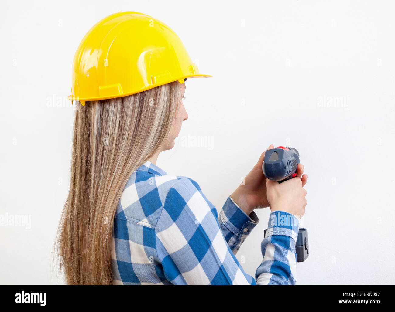 Junge Frau ein Loch in die Wand bohren und einen Schutzhelm tragen Stockfoto