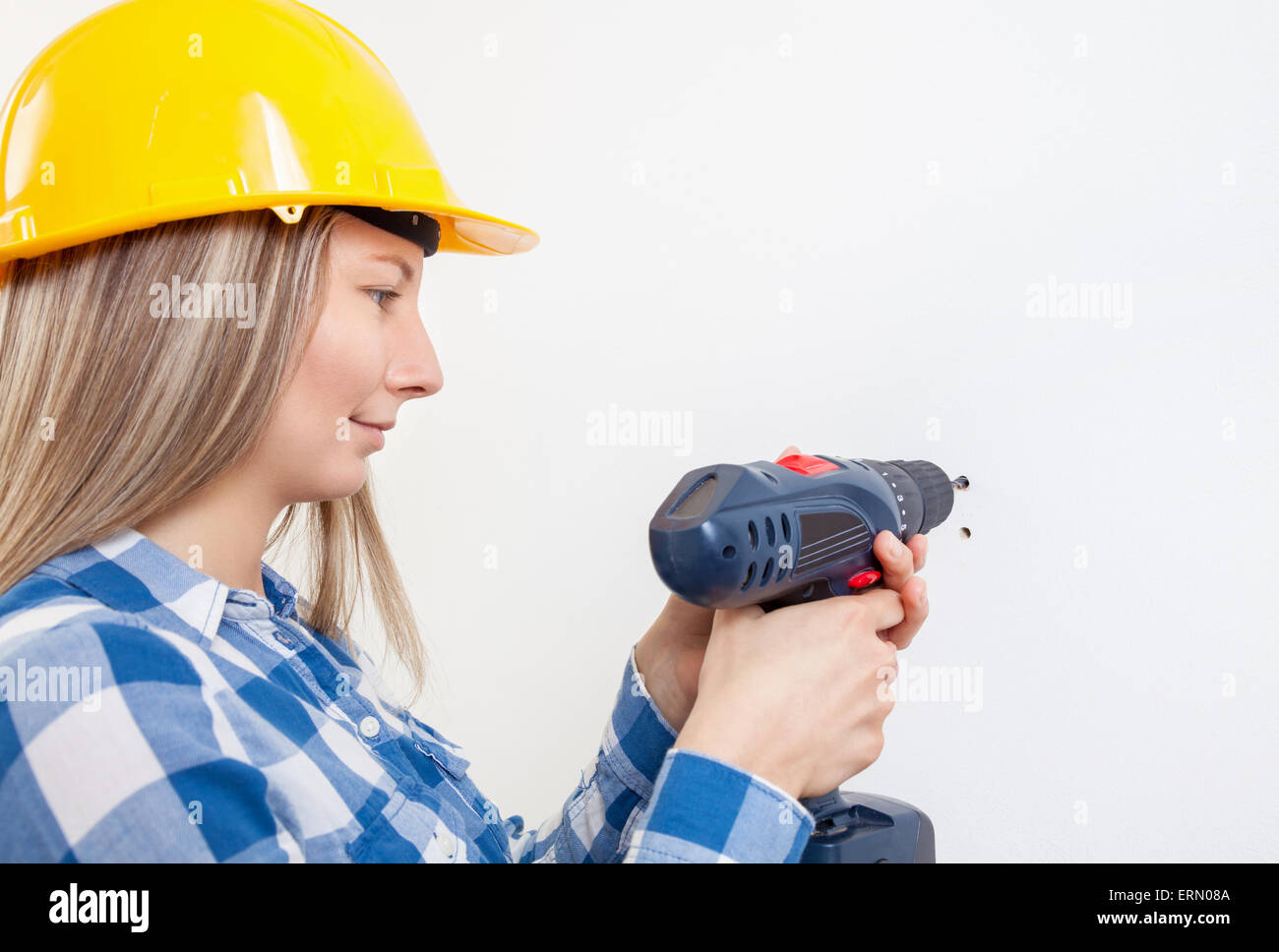 Junge Frau ein Loch in die Wand bohren und einen Schutzhelm tragen Stockfoto