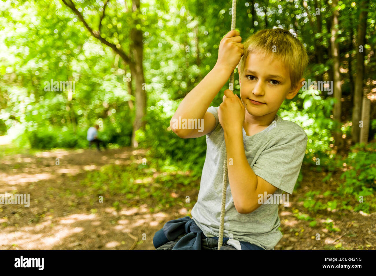 Blonde Junge an der Schaukel sitzend in Holz Stockfoto