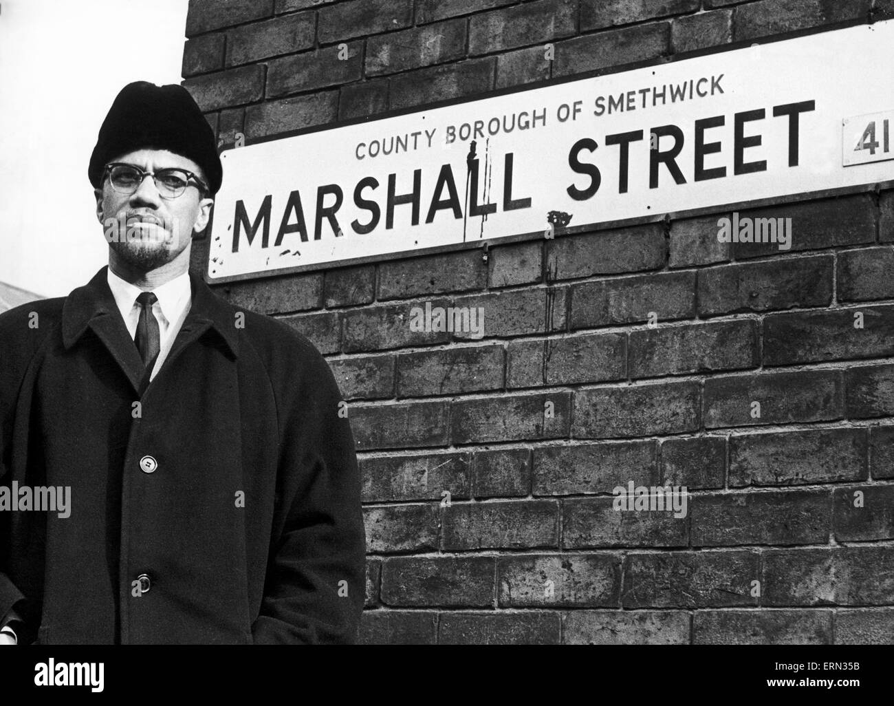 Malcolm X afro-amerikanischen muslimischen Minister und Menschenrechte Aktivisten Posen neben dem Straßenschild für Marshall Street in Smethwick bei einem Besuch in den Midlands. Der Menschenrechtler stellte neben dem Typenschild, ging 50 Yards die Straße hinauf, lächelte Stockfoto