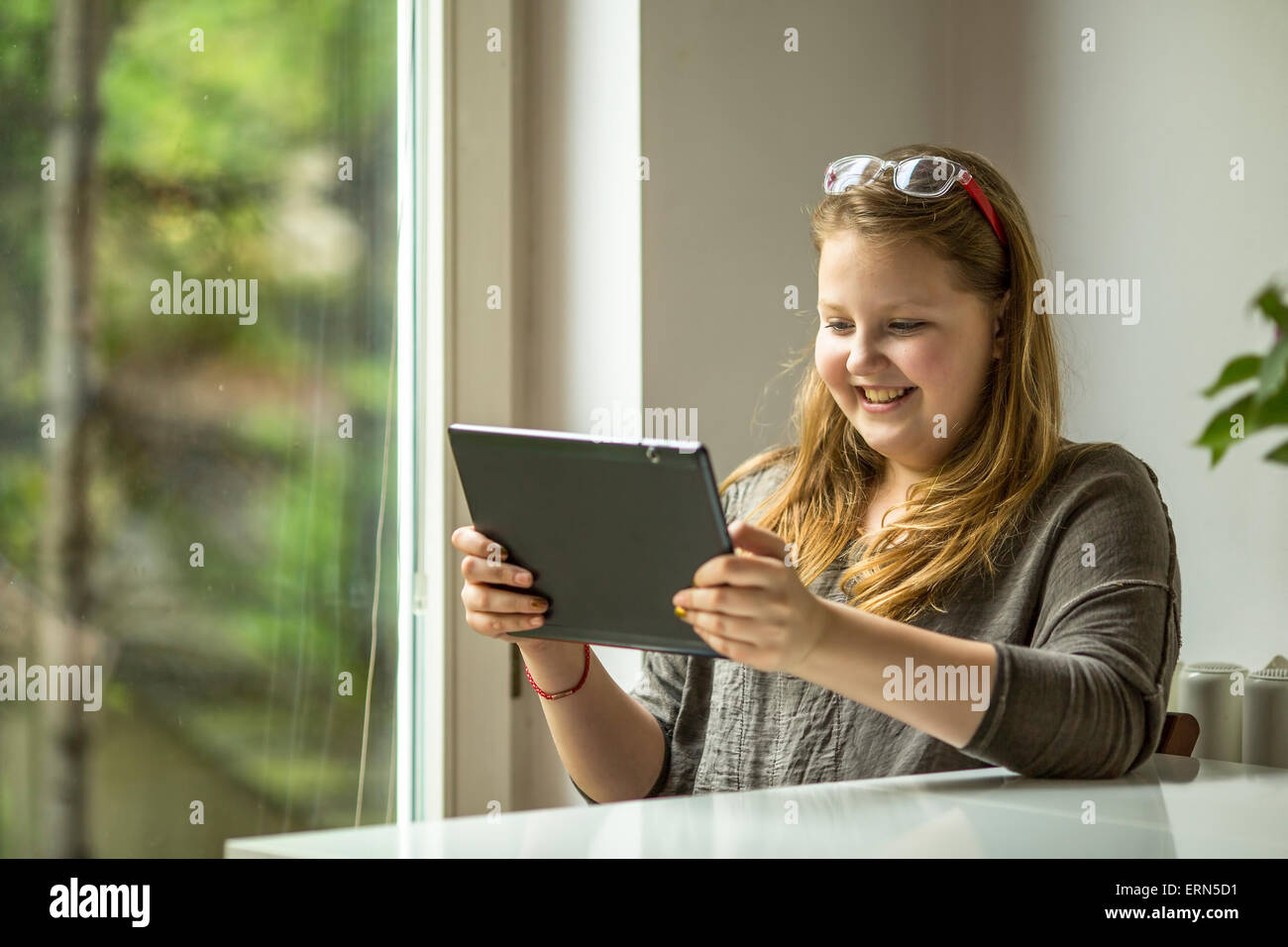 Teenager-Mädchen mit Tablet in Händen sitzt an einem Tisch am Fenster. Stockfoto
