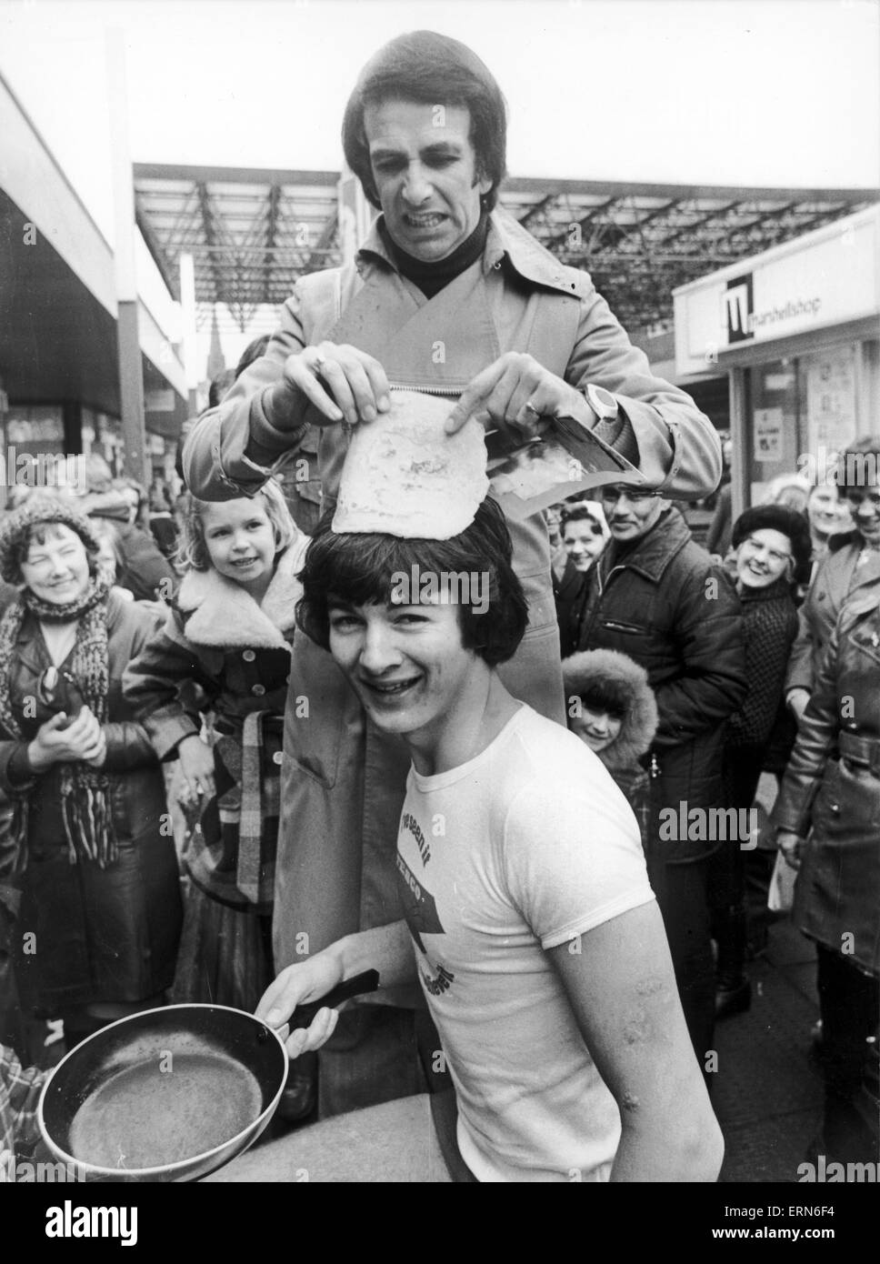 Paul Irvine, Trainee Manager bei Tesco, fand sich seine Pfannkuchen als Hut versucht, beim Birmingham-Komiker und Schauspieler Don Maclean ihn mit seinen Preis für den Gewinn der Mens Pancake Race, Sandwell Mail, Birmingham, 22. Februar 1977 vorgestellt. Stockfoto