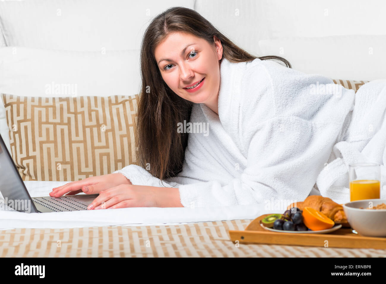 schönes Mädchen mit einem Laptop im Bademantel auf dem Bett Stockfoto