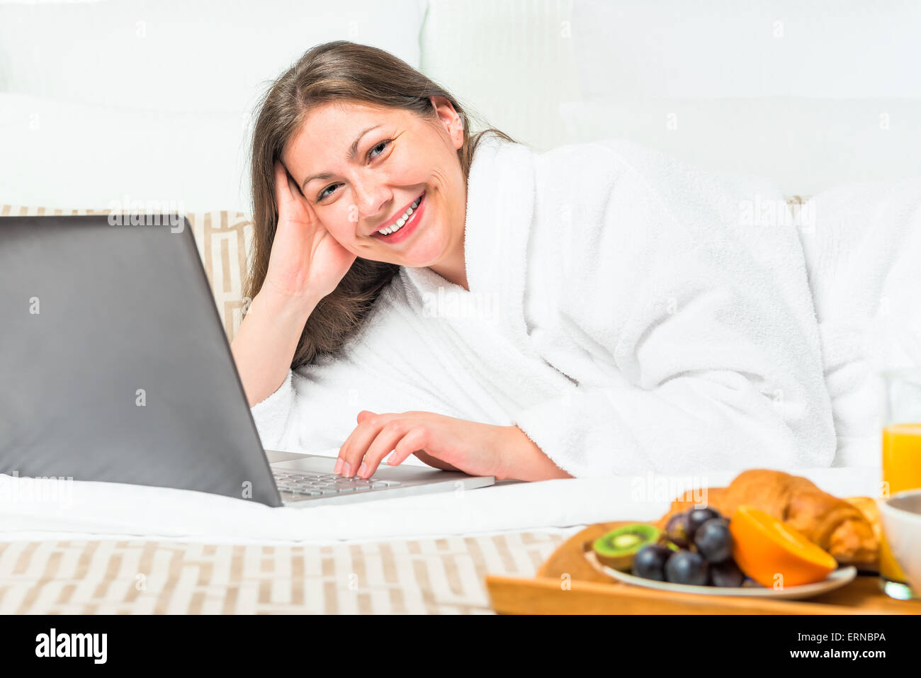lächelnde Frau im Bett mit einem Laptop und Frühstück Tablett Stockfoto