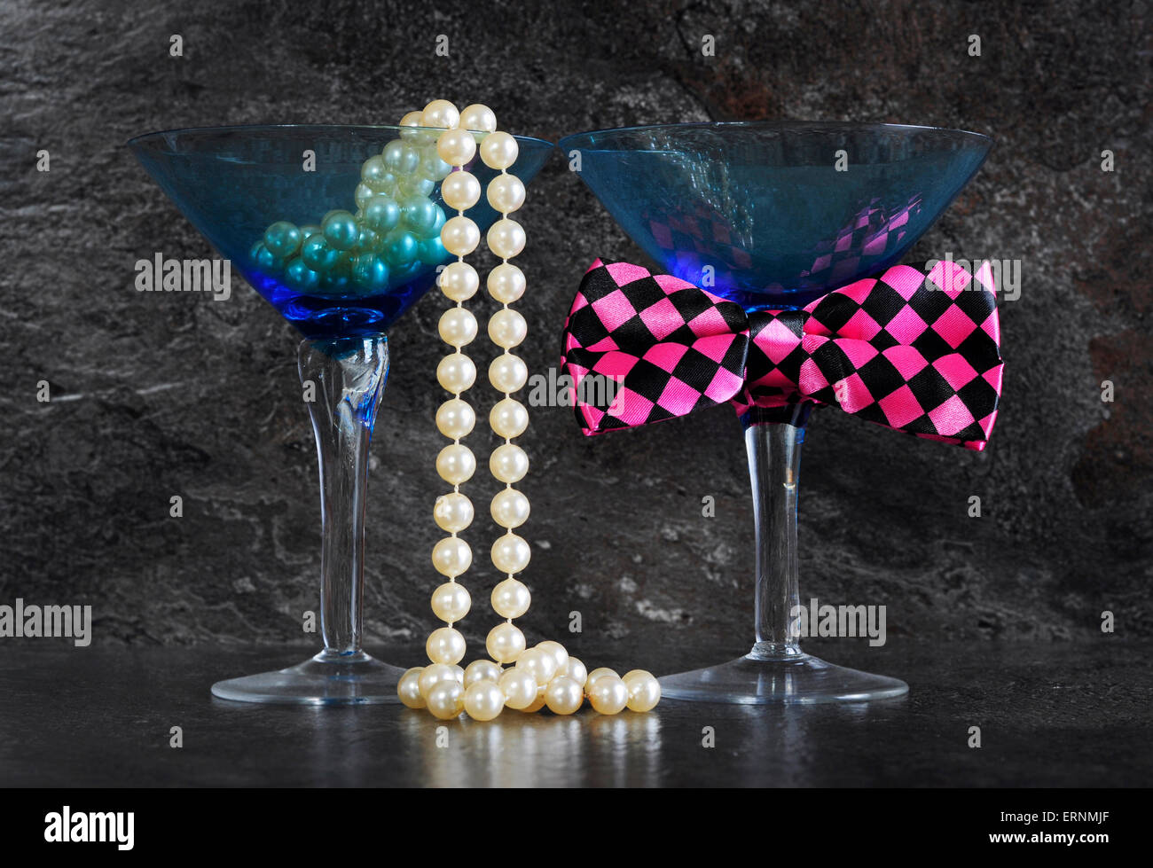 Ladies und Gentleman Vintage blue Martini-Gläser mit Perlen und Spaß rosa prüfen Fliege auf schwarzem Schiefer Hintergrund. Stockfoto