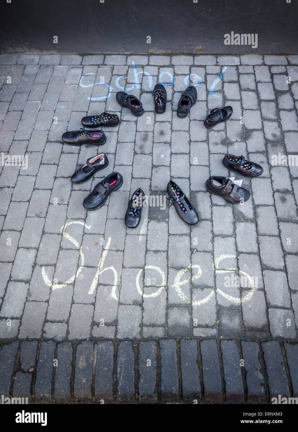 12 neue schwarze Schulschuhe in einem Kreis auf dem Bürgersteig mit den Worten Schule Schuhen platziert Kreide auf dem Boden Stockfoto